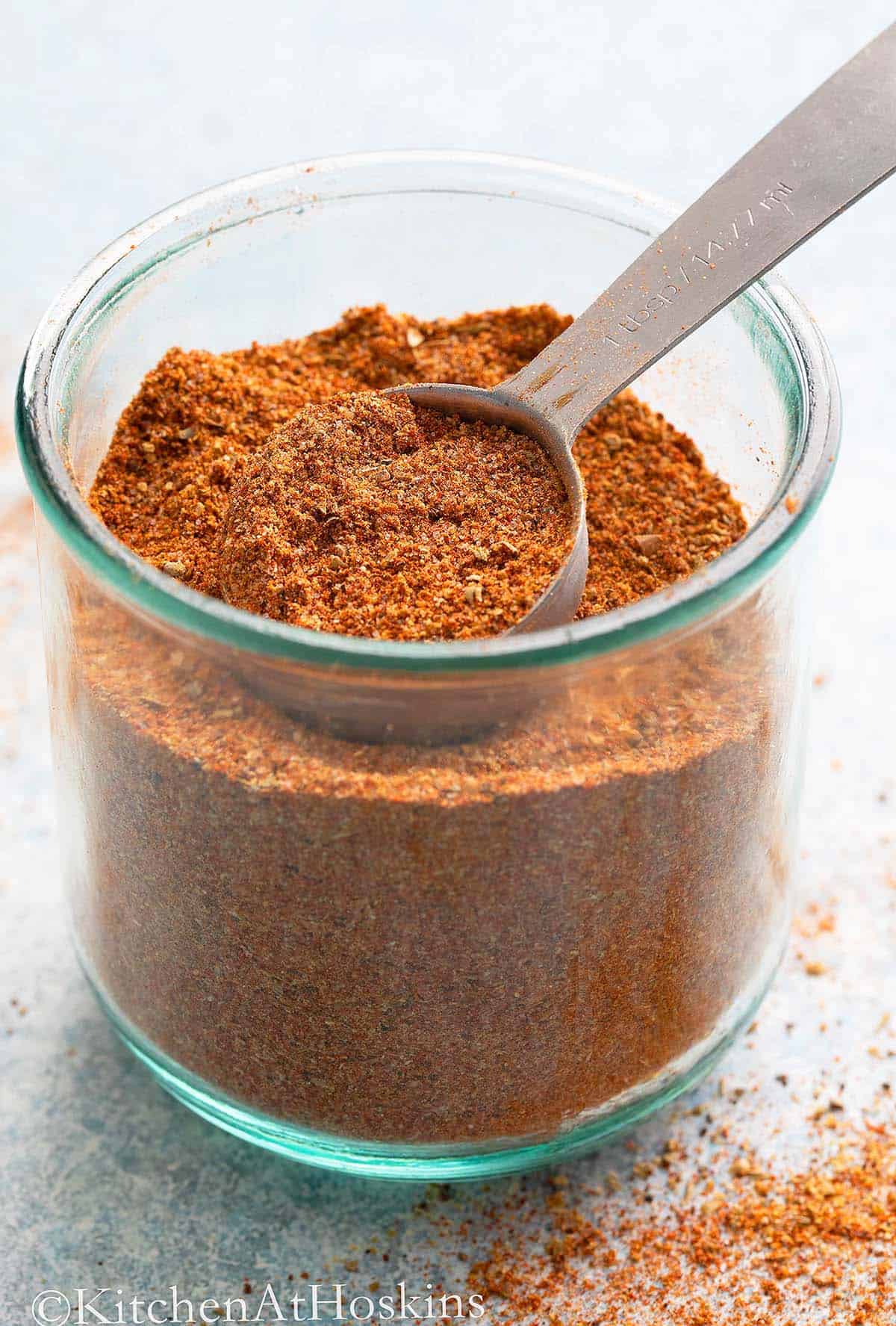 red colored ground spices in a glass jar along with a tablespoon.