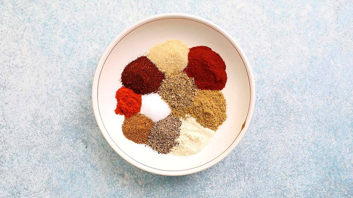 10 different spices placed in a round white dish.