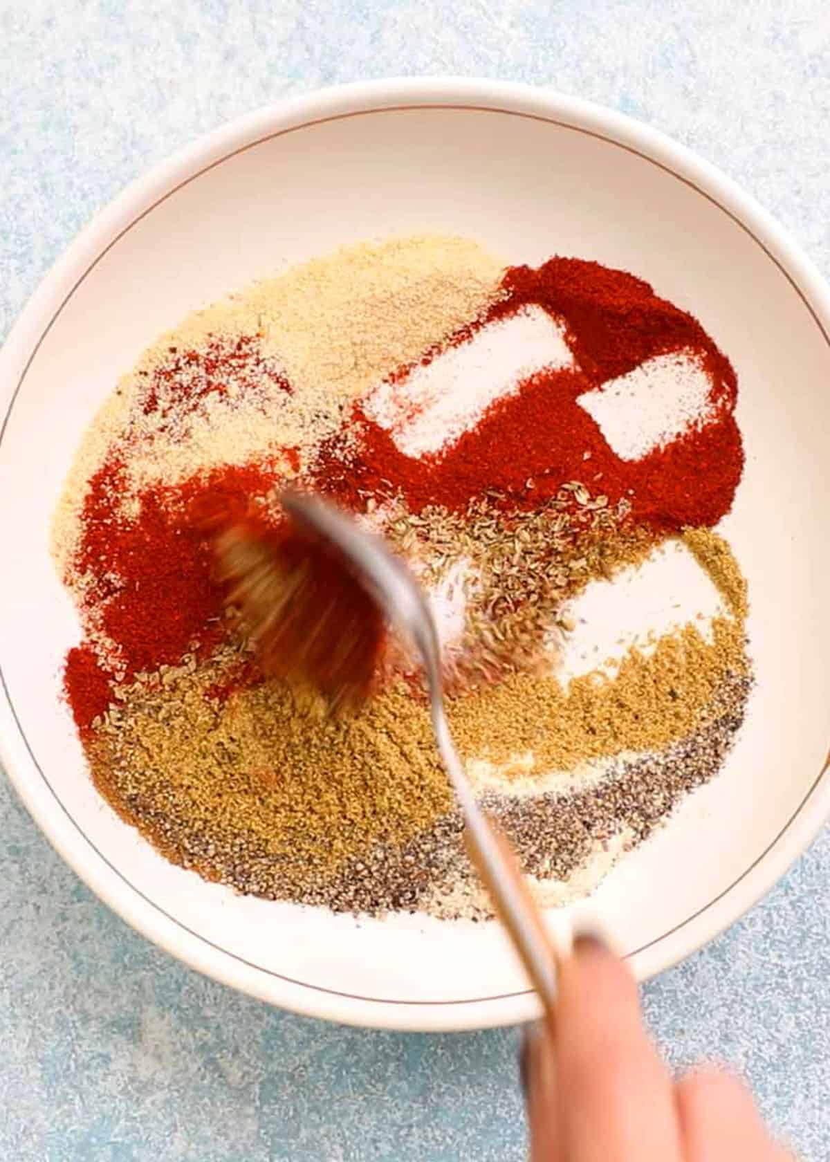 a hand stirring ground spices in a white plate.
