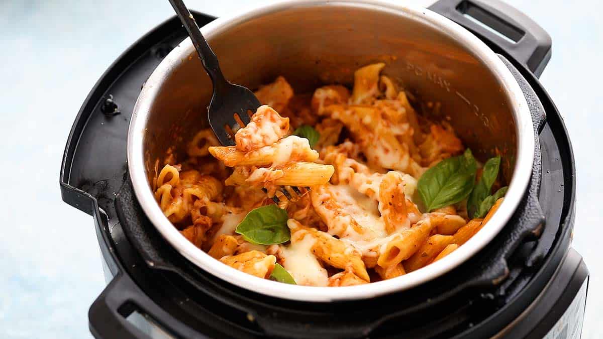 an instant pot filled with cooked pasta topped with cheese and basil. 