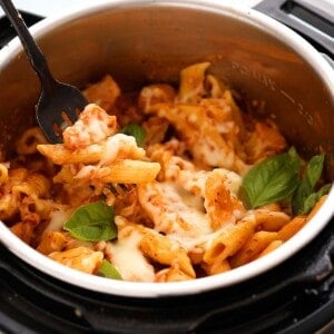 a black fork with a bite of chicken and cooked penne pasta on top of an instant pot.