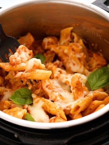 a black fork with a bite of chicken and cooked penne pasta on top of an instant pot.