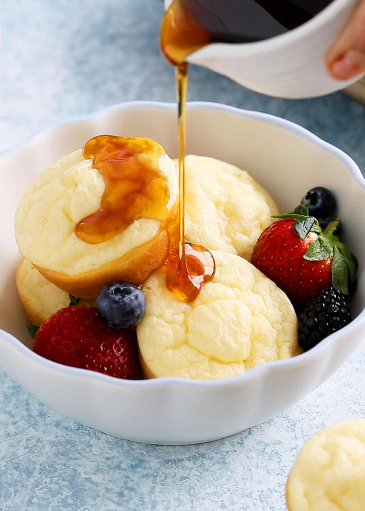 4 pancake cups in a white bowl topped with maple syrup.