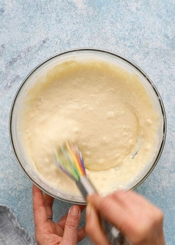 two hand whisking pancake batter in a glass bowl.