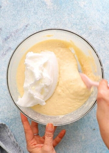 two hand mixing pancake batter in a glass bowl.