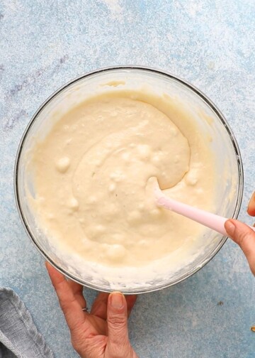 two hand whisking pancake batter in a glass bowl.