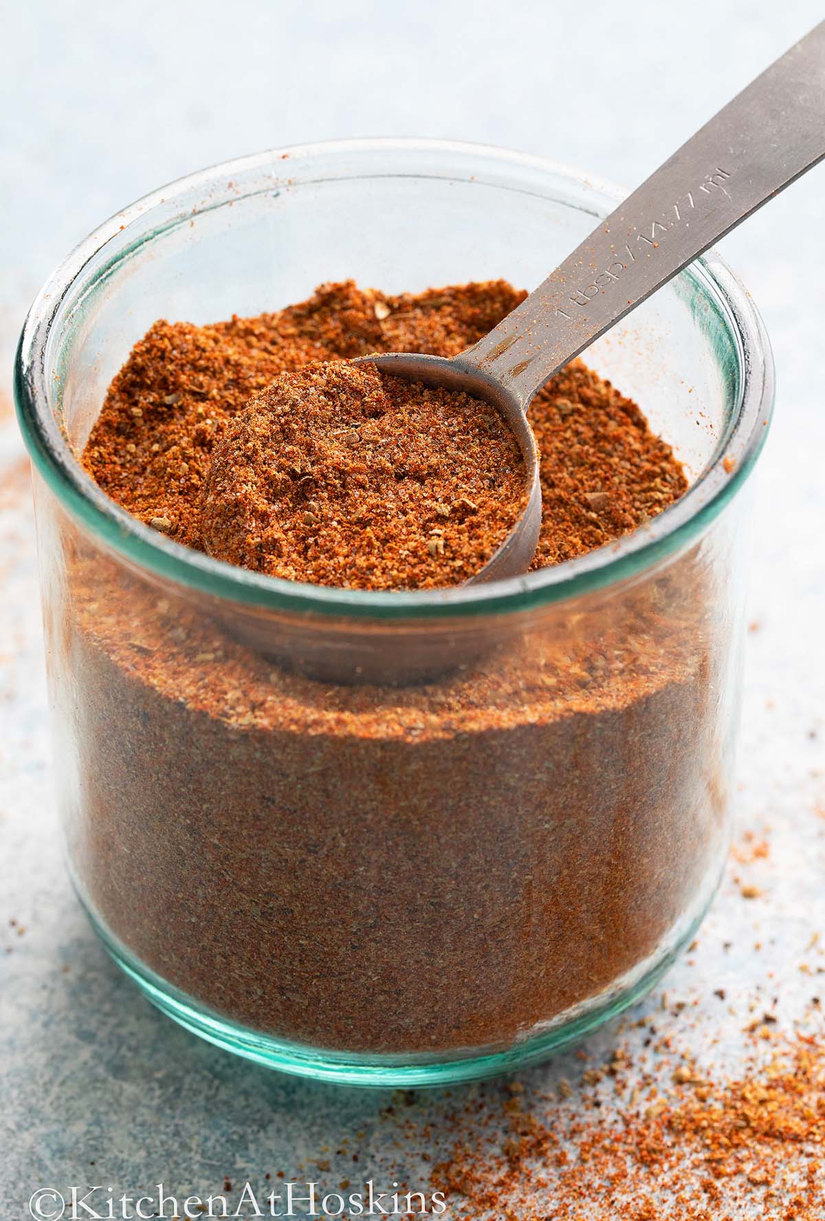 glass jar with taco seasoning along with a tablespoon.
