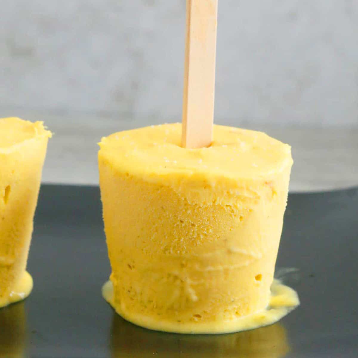 one mango popsicle in a black plate.