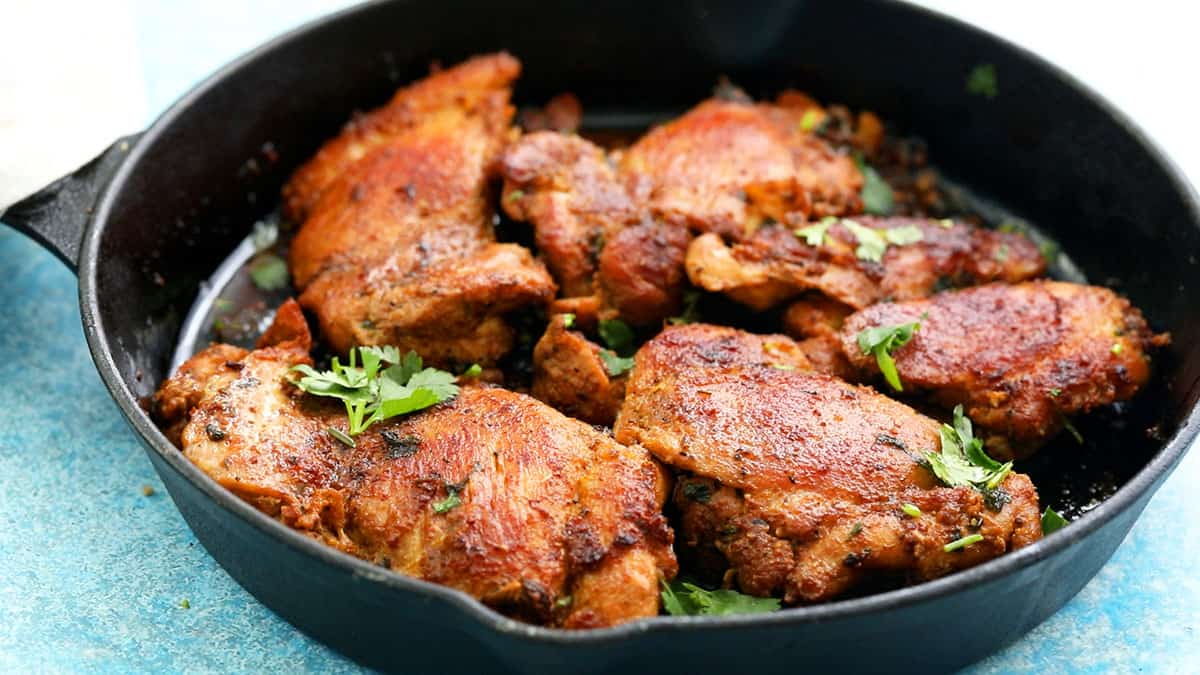 cooked brown chicken thighs placed in a black skillet.
