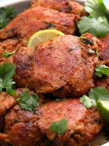 cooked brown chicken thighs placed in a round plate.