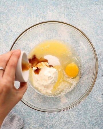 a hand adding vanilla extract into a  large glass bowl.