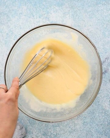 a hand whisking wet ingredients in a glass bowl.