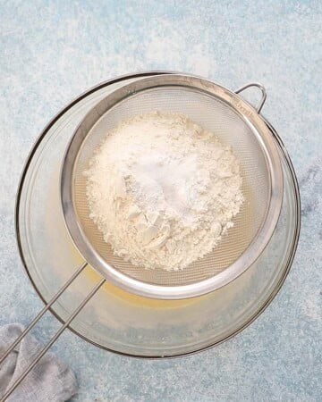 a strainer with white flour placed on top of a glass bowl.