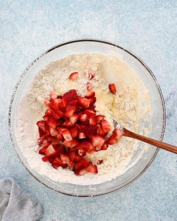 chopped red strawberries along with muffin batter in a glass bowl.