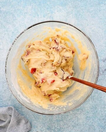 chopped red strawberries along with muffin batter in a glass bowl.