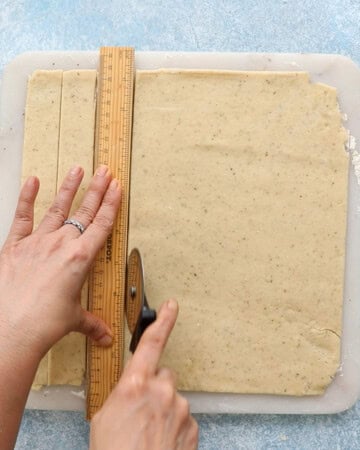 two hands cutting squares from a rolled sheet of dough.