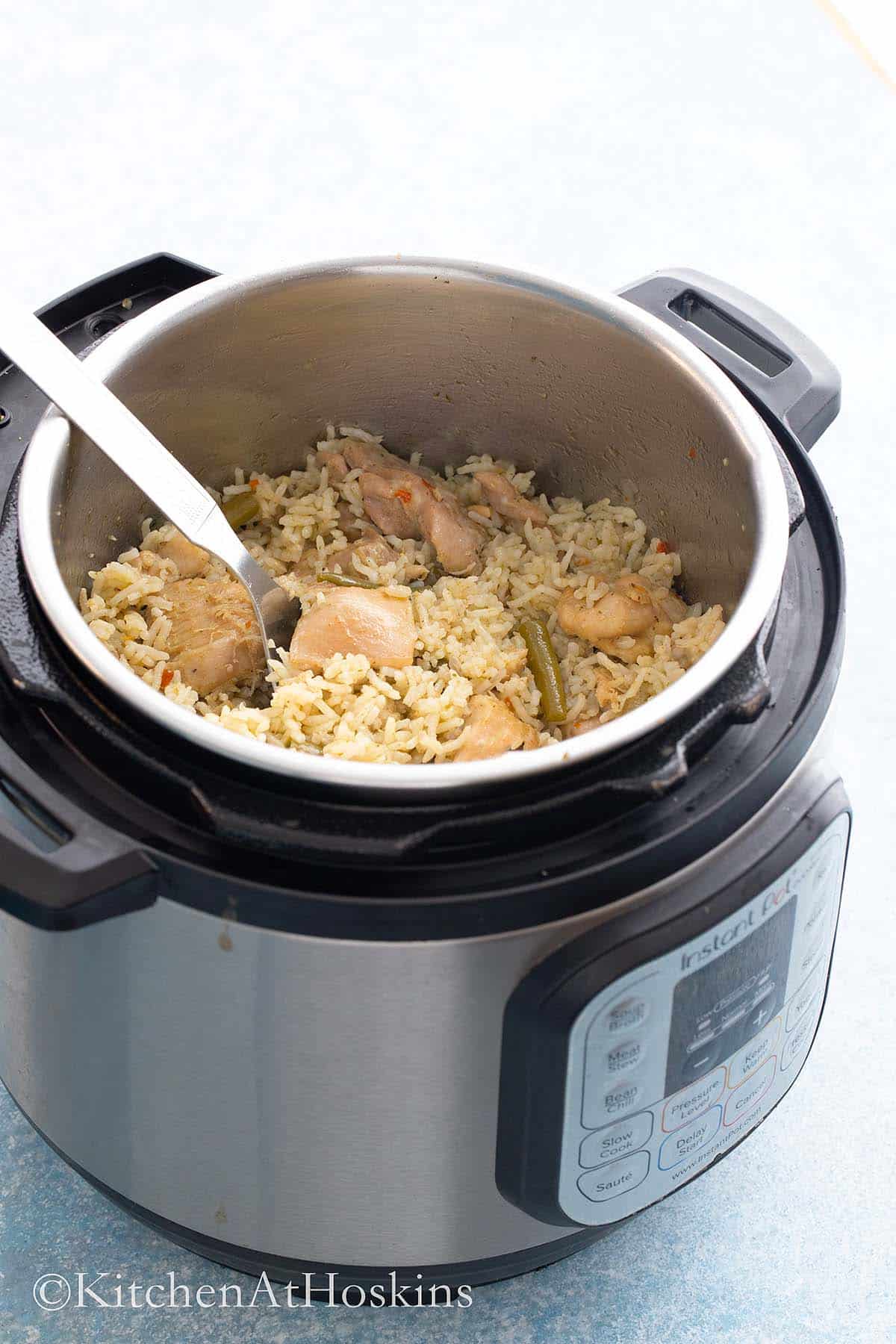 instant pot with chicken and rice along with a stainless steel spoon. 