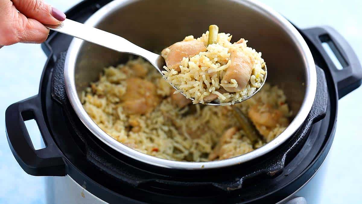 a stainless steel spoon full of chicken and rice above an instant pot. 