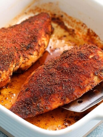 2 baked chicken breasts in a white baking dish.