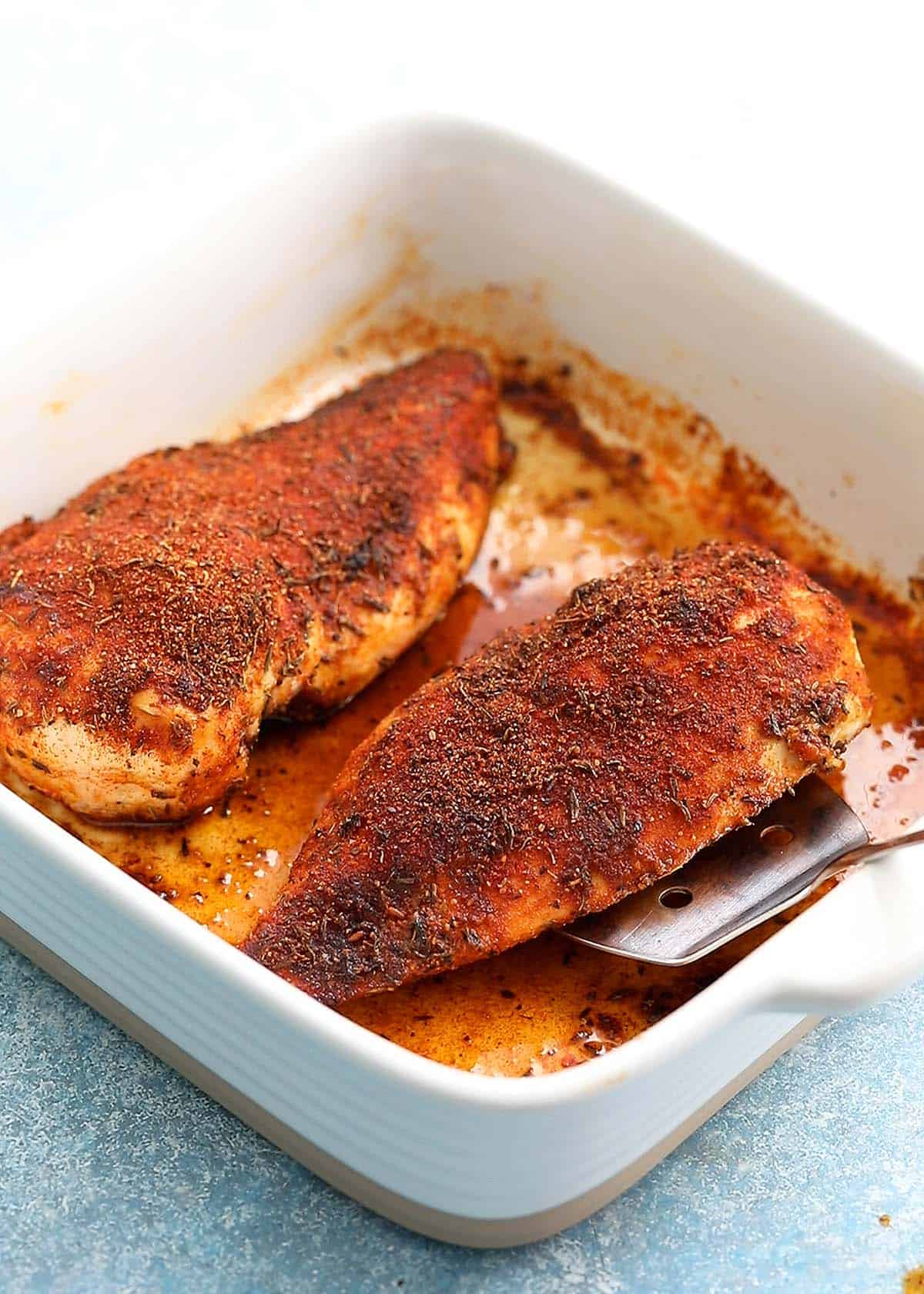 2 cooked chicken breasts on a white ceramic baking dish.