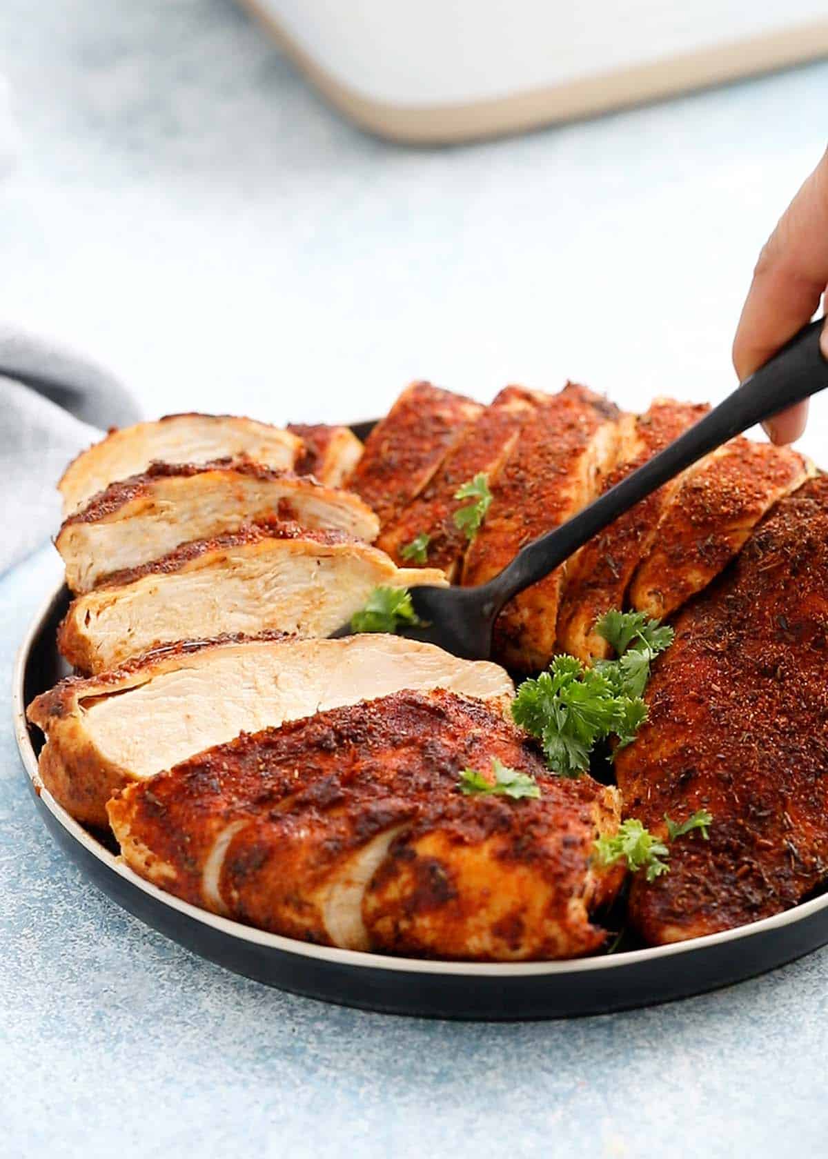 a fork lifting off a piece of sliced chicken breast from a black plate.