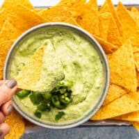 a hand dipping a chip in a bowl of avocado crema.