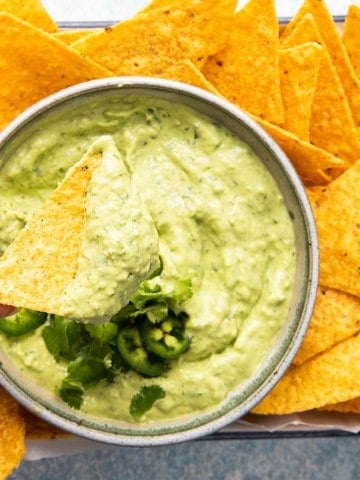 a hand dipping a chip in a bowl of avocado crema.