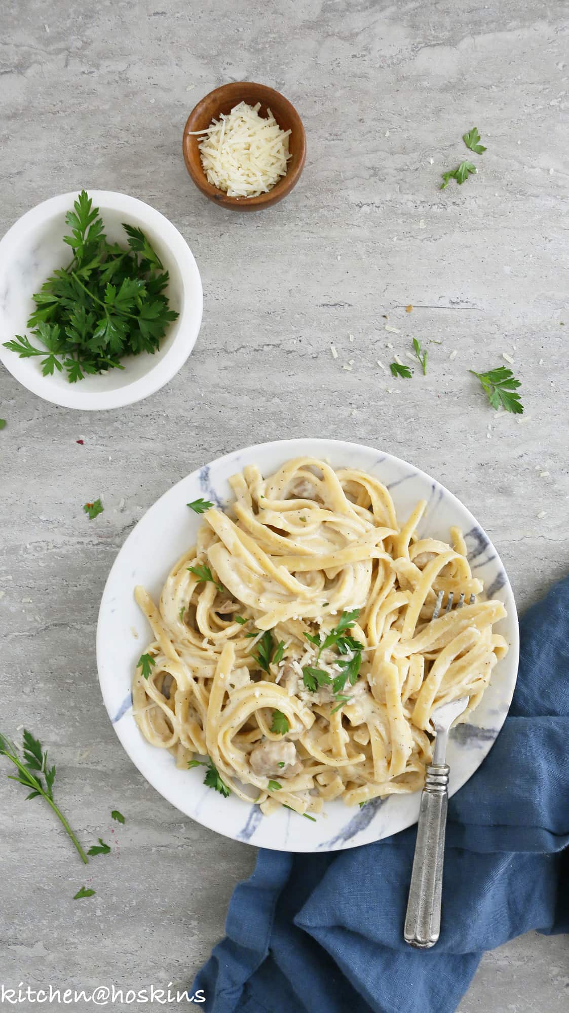 chicken alfredp pasta served on a plate with a silver spoon and grated parmesan and fresh parsley for garnish