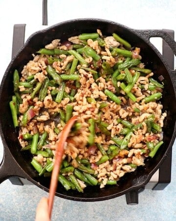 a hand cooking chicken and green beans in a black skillet.