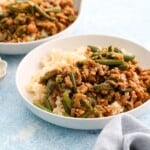 cooked chicken and green beans along with white rice in two white bowls.