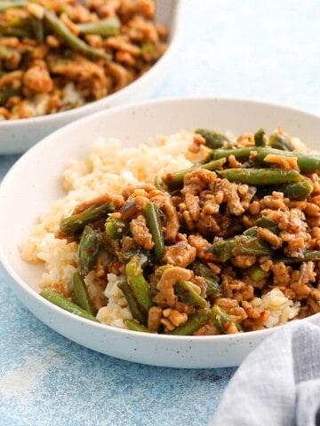 cooked chicken and green beans along with white rice in two white bowls.