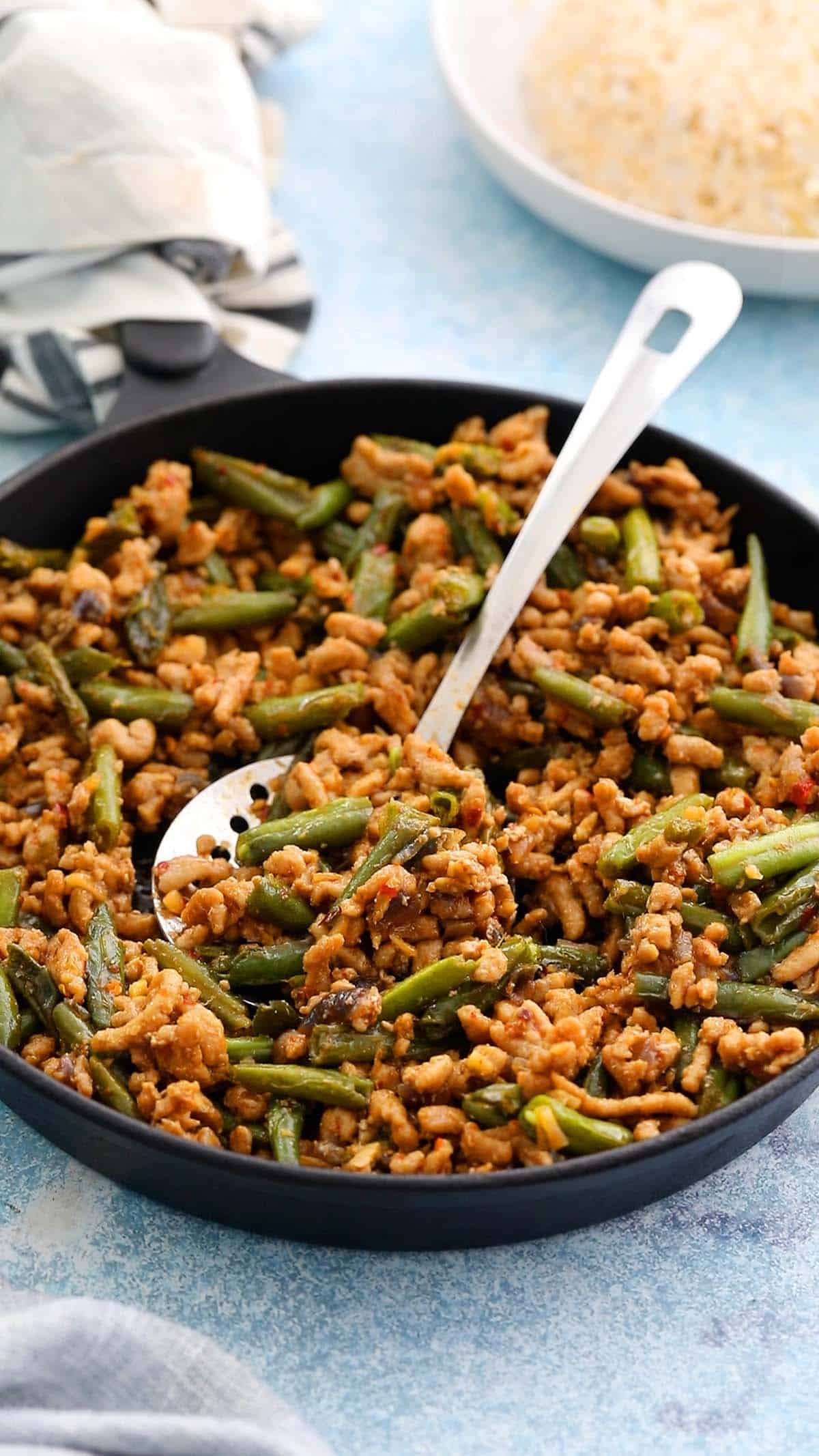 cooked chicken and green beans stir fry in a black skillet.