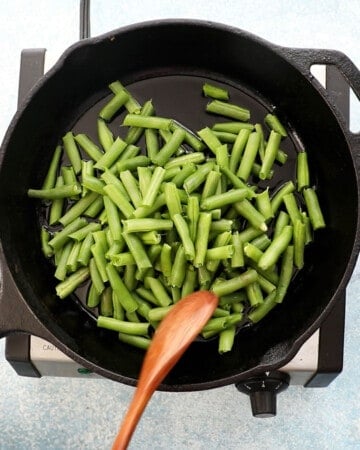 a hand cooking chopped green beans in a black skillet. 