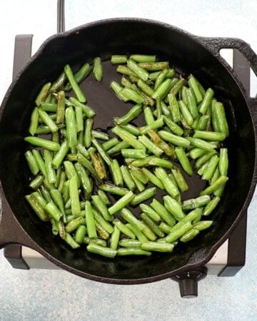a hand cooking chopped green beans in a black skillet. 