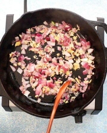 a hand cooking chopped onion, ginger and garlic in a black skillet.