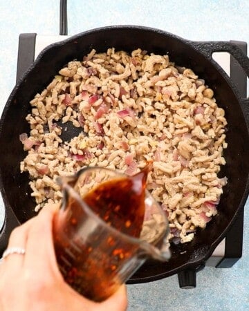 a hand pouring sauce over cooked chicken in a black skillet.