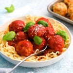 spaghetti and chicken meatballs garnished with green basil leaves in a white plate.