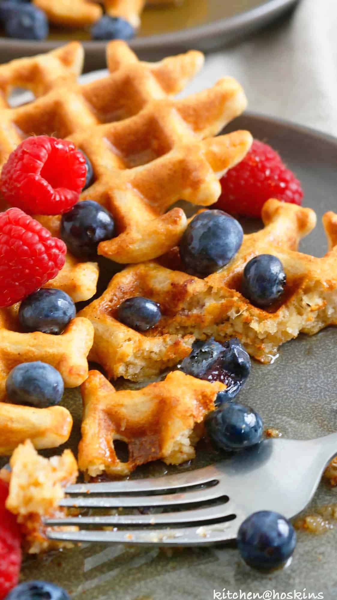 half eaten waffle on a grey plate with fork.