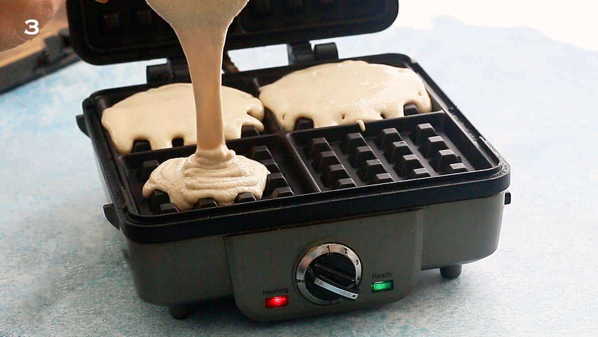 a hand pouring waffle batter into a waffle maker.