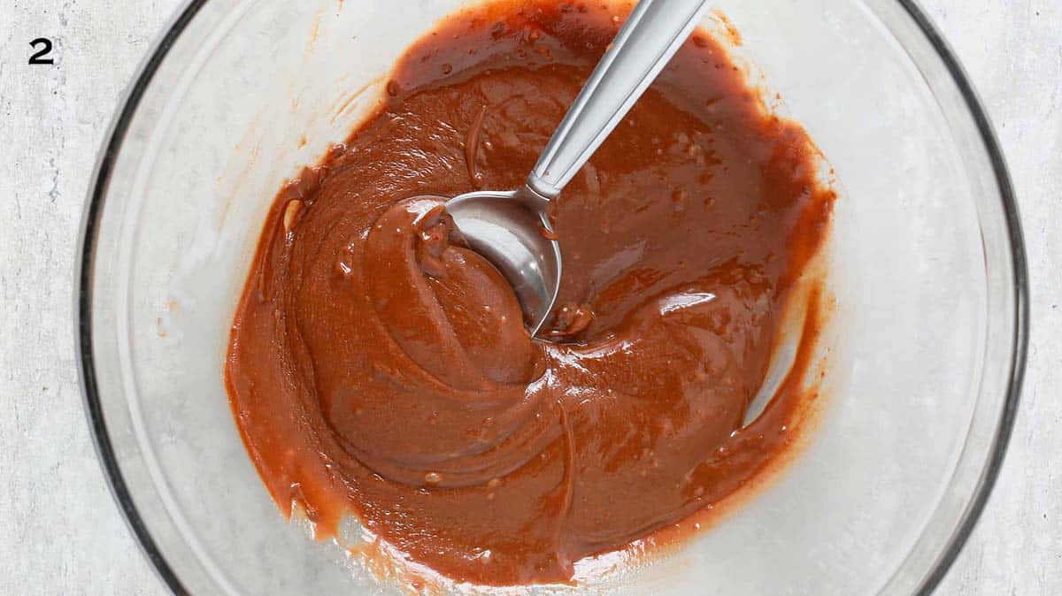 a stainless steel spoon in a glass bowl with melted chocolate.