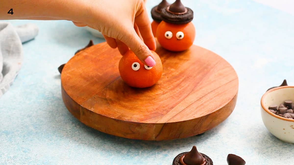 a hand sticking candy eyeballs on cleemntines.