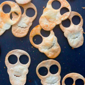Halloween themed tortilla chips in the shape of skulls on a black board.