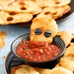 one skull shaped chip half immersed in salsa, placed in a small black bowl.