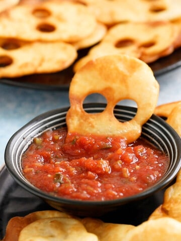 one skull shaped chip half immersed in salsa, placed in a small black bowl.