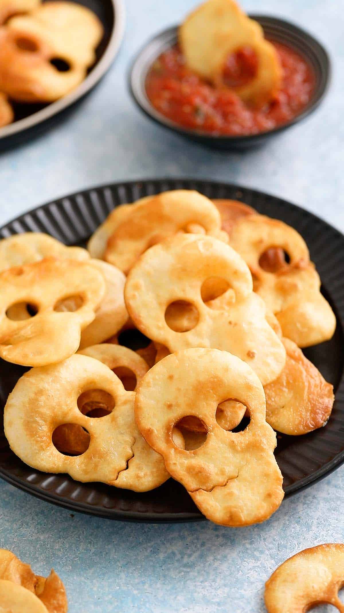 Skull shaped tortilla chips piled on a round black plate.
