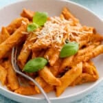 pink pasta topped with green basil in a white bowl.