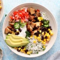 assembled chicken burrito bowl in a white bowl along with sliced avocado.