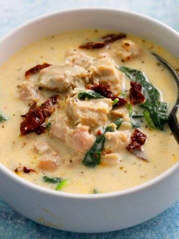 white chicken soup with green spinach leaves in a white bowl with one black spoon.