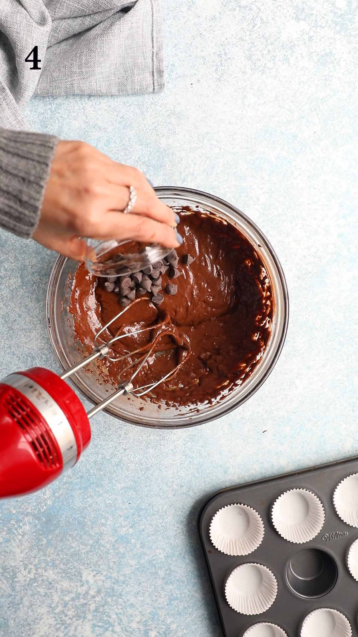 a hand adding chocolate chips into a glass bowl.