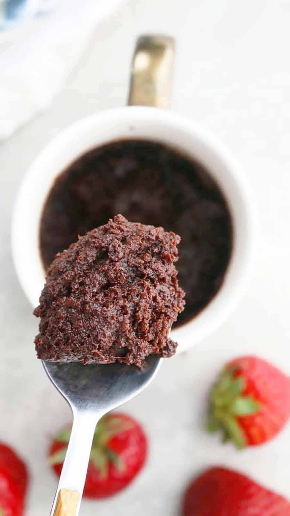 a spoonful of chocolate cake above a white mug.